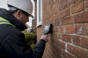 Surveyor inspecting UK brick cavity wall with metal detector